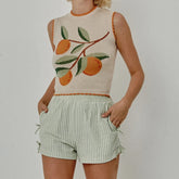 Person wearing a sleeveless top with fruit design and shorts on a plain background